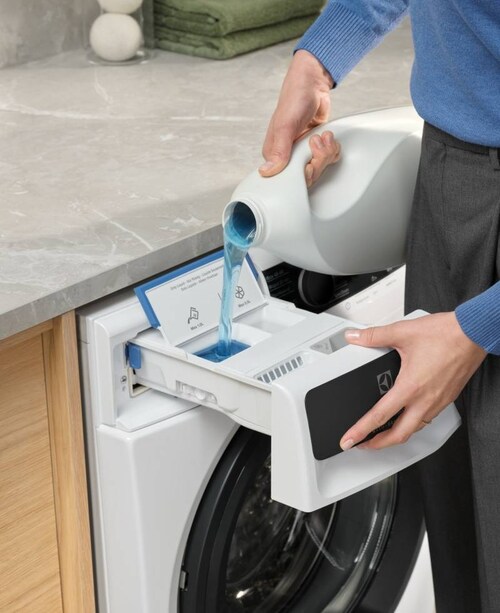 Henkilö annostelee pesuainetta Electroluxin pesukoneeseen.
