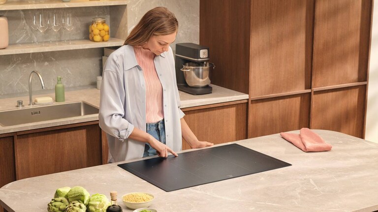 Nainen laittaa ruokaa keittotason äärellä. 