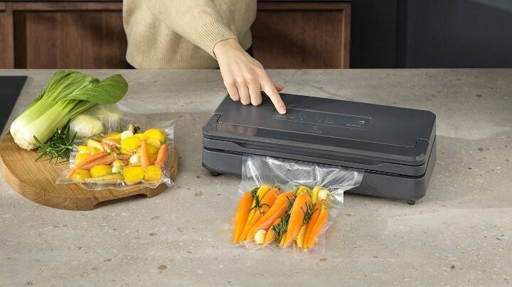 Henkilö tyhjiöpakkaa porkkanoita tyhjiöpakkauslaitteella. 