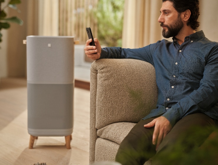 Mies, joka pitää puhelinta kädessään istuen ilmanpuhdistimen vieressä