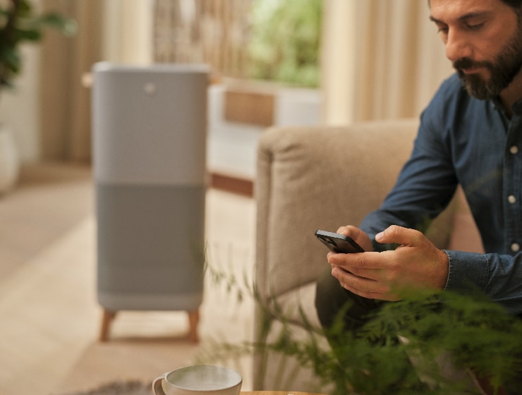 Mies, joka pitää puhelinta kädessään istuen ilmanpuhdistimen vieressä.