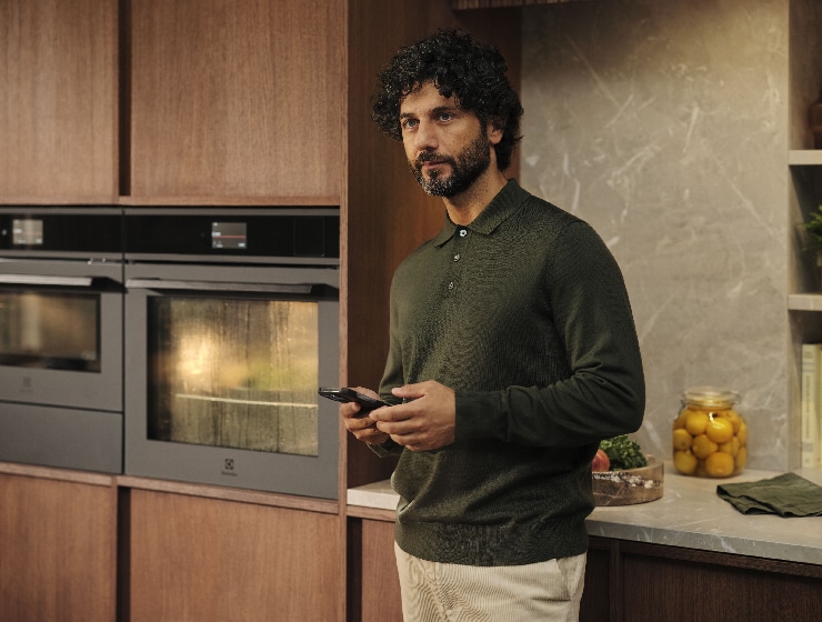 Mies seisoo keittiössä puhelimen kanssa kädessään