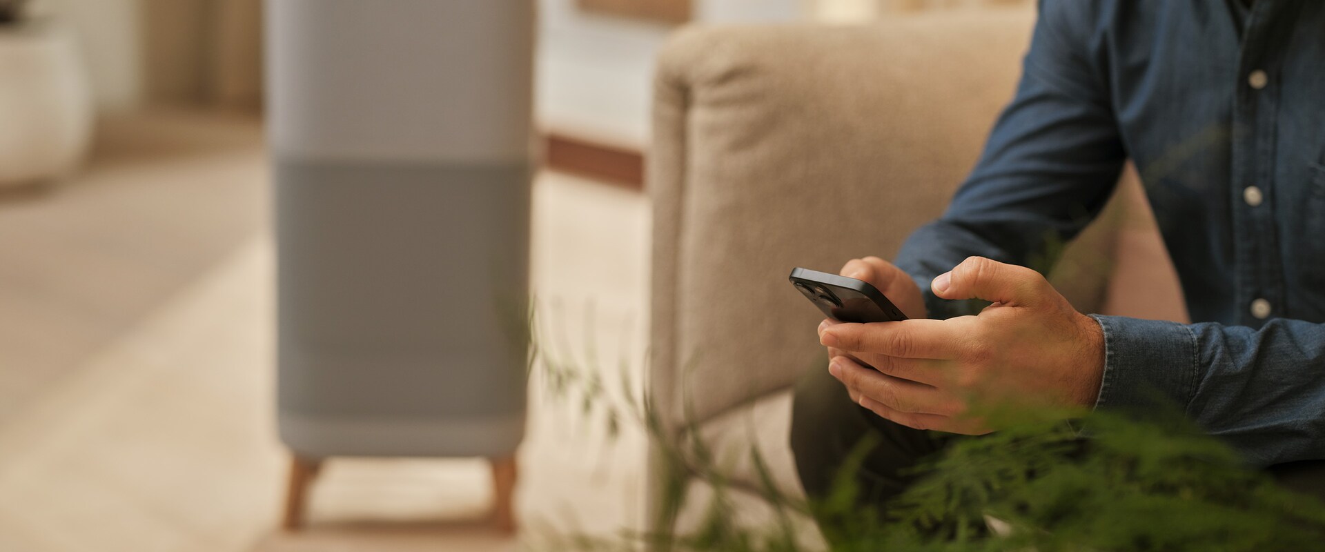 Mies sohvalla puhelimen kanssa. Ilmanpuhdistin taustalla.