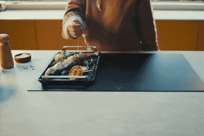 A person is squeezing a lemon over the food on an induction hob.