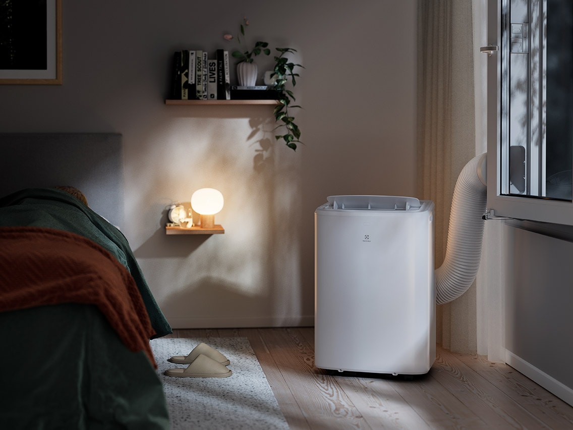 Valkoinen, kannettava Electrolux-ilmastointilaite, joka on yhdistetty makuuhuoneen ikkunaan.