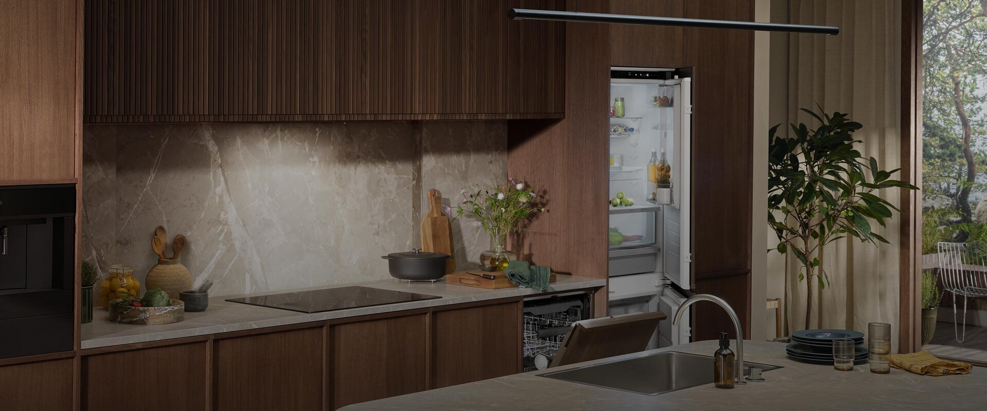 Integroitu jääkaappipakastin ja astianpesukone tyylikkäässä keittiössä, jossa on tummat puupaneelit ja marmorityötaso.