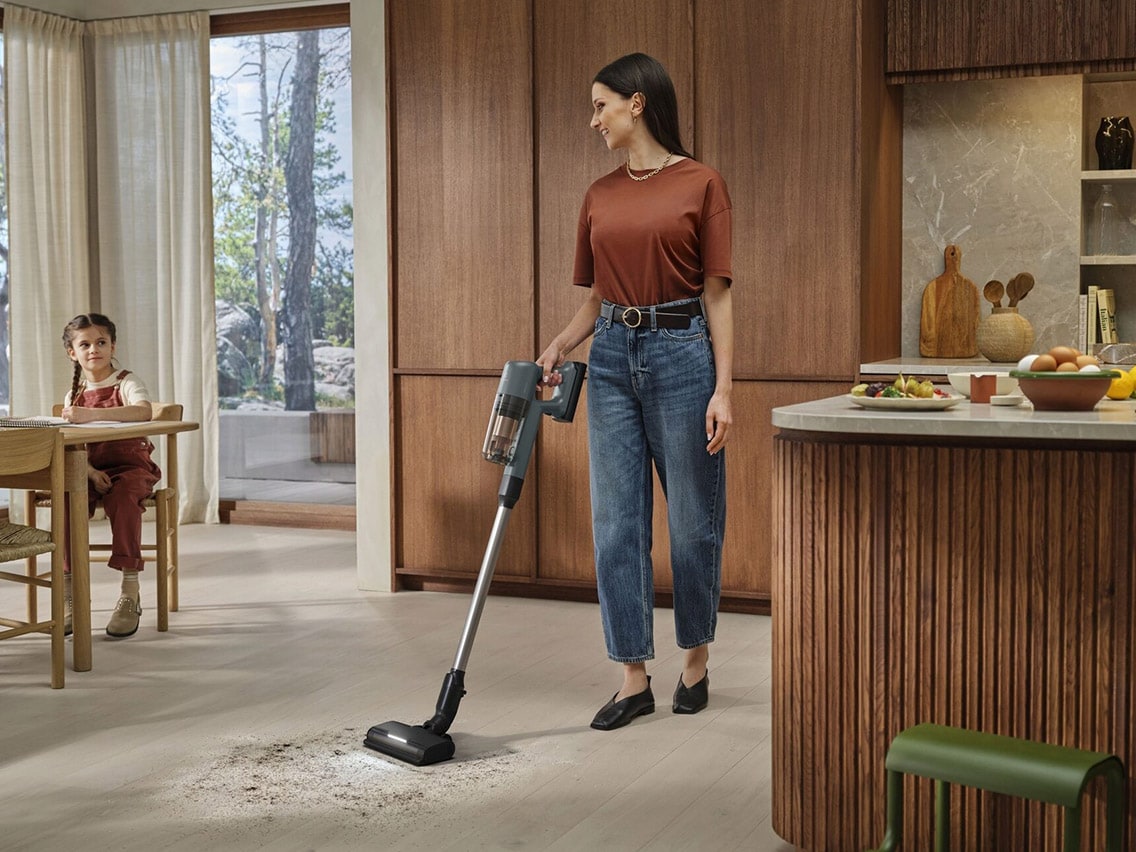 Nainen siivoaa modernin keittiön vaaleaa puulattiaa langattomalla Electrolux 700 -imurilla.