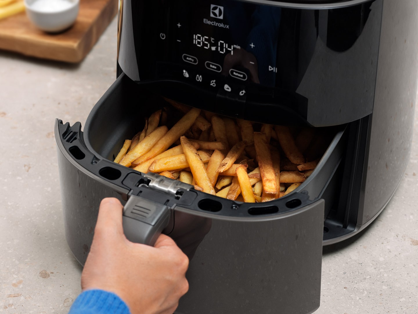 Nytillagade pommes frites plockas ut ur en Airfryer.