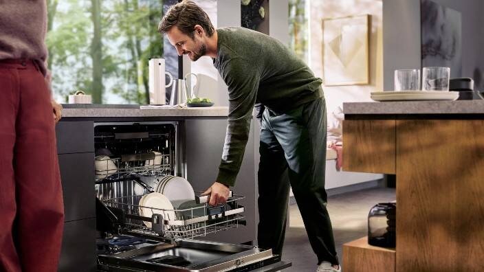 Henkilö tyhjentää tiskikonetta keittiössä.