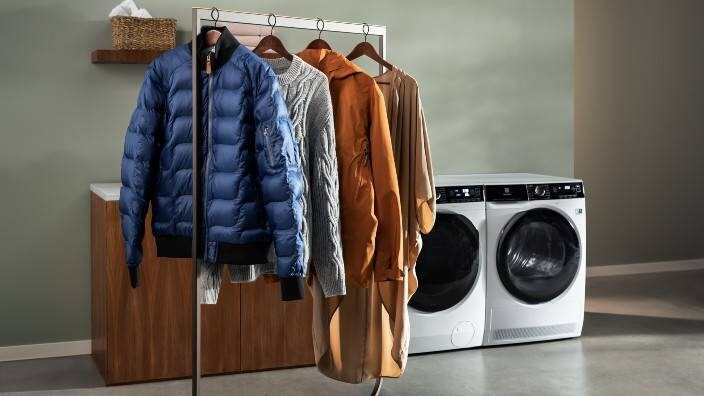 Vaatteita ripustettuna Electroluxin pesukoneen ja kuivausrummun eteen.